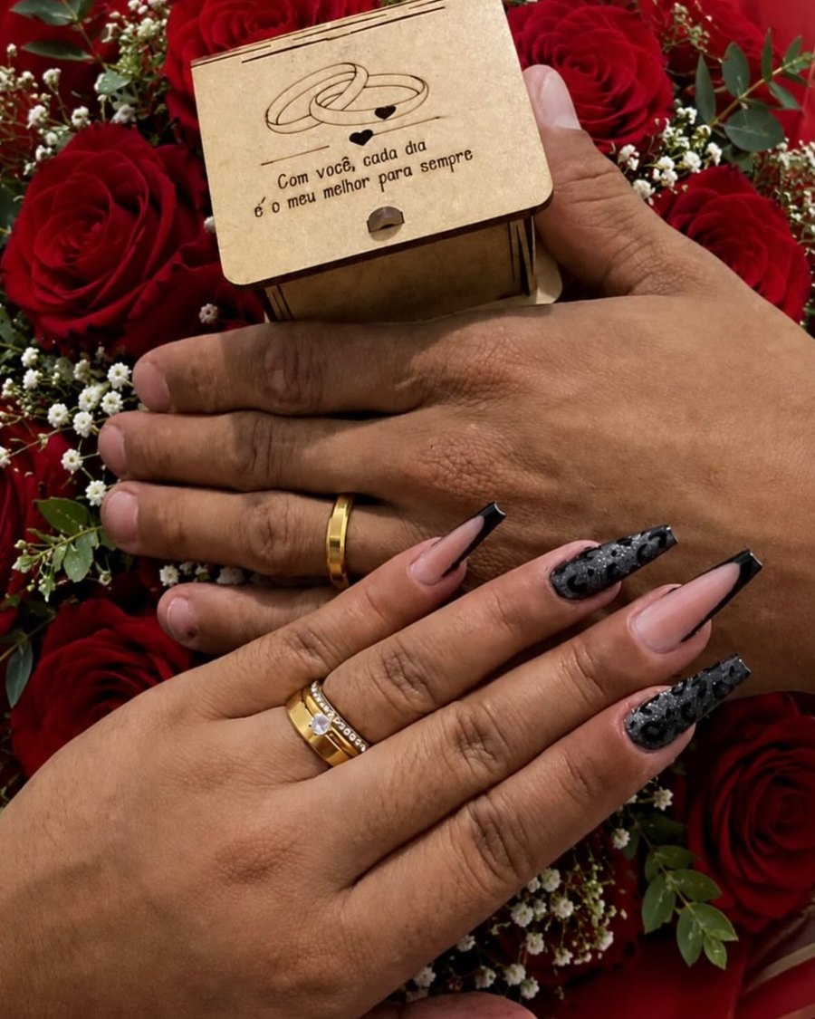 Mão com unhas decoradas segurando uma caixinha de aliança sobre rosas vermelhas
